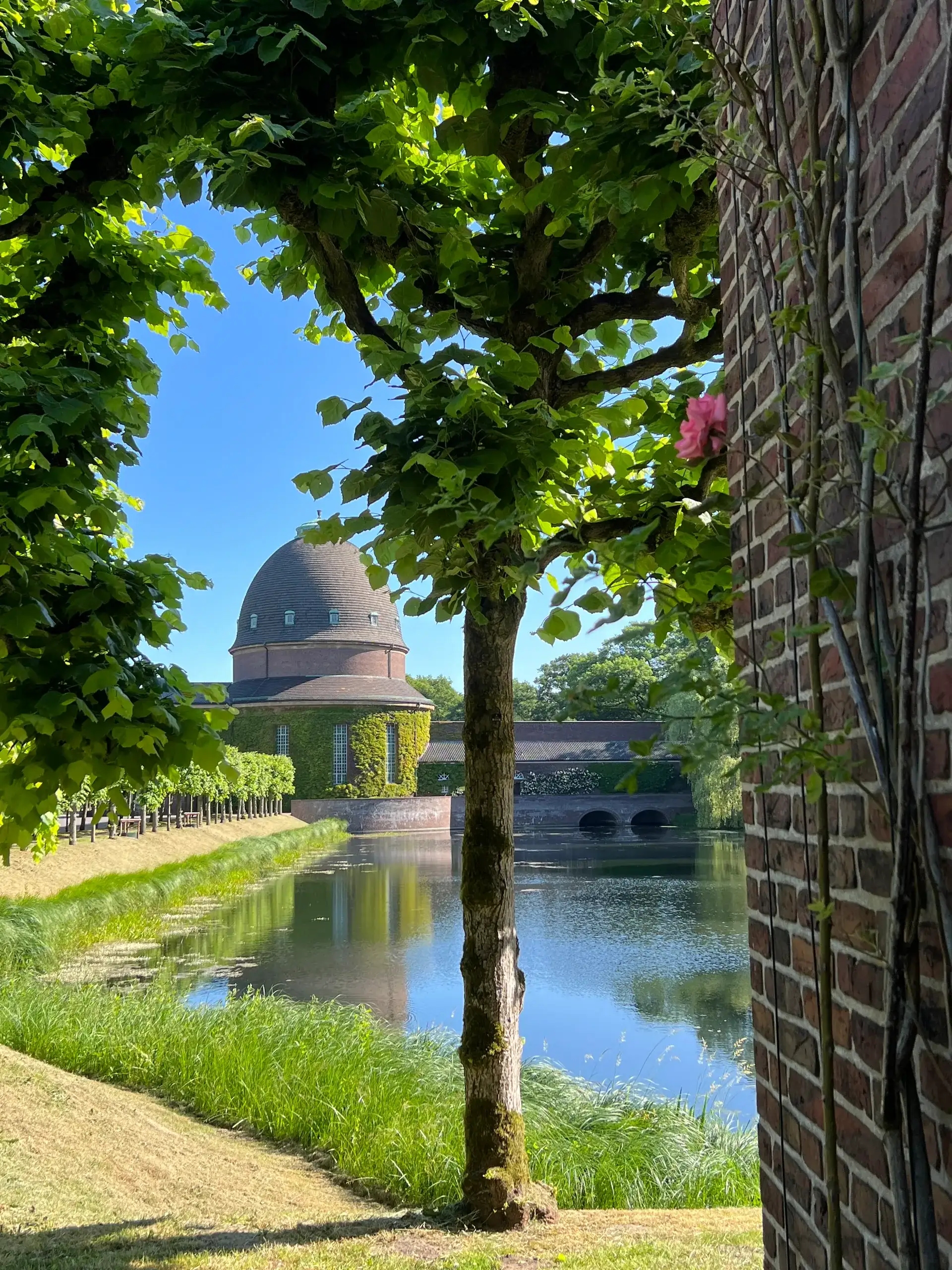 Kapelle mit Kuppeldach an einem Wassergraben, von alten Bäumen gerahmt