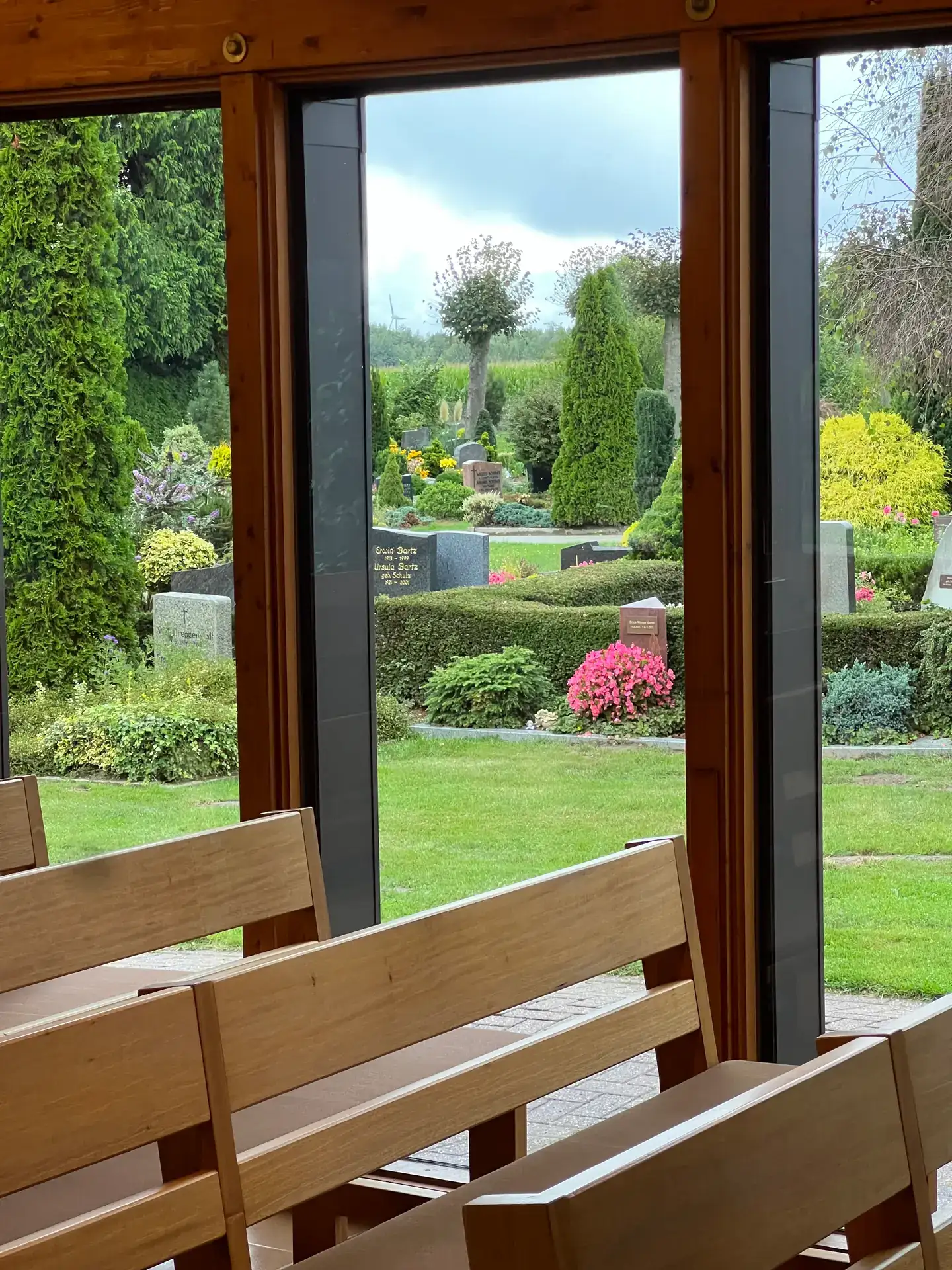 Blick aus der Trauerhalle durch große Fenster auf den begrünten Friedhof