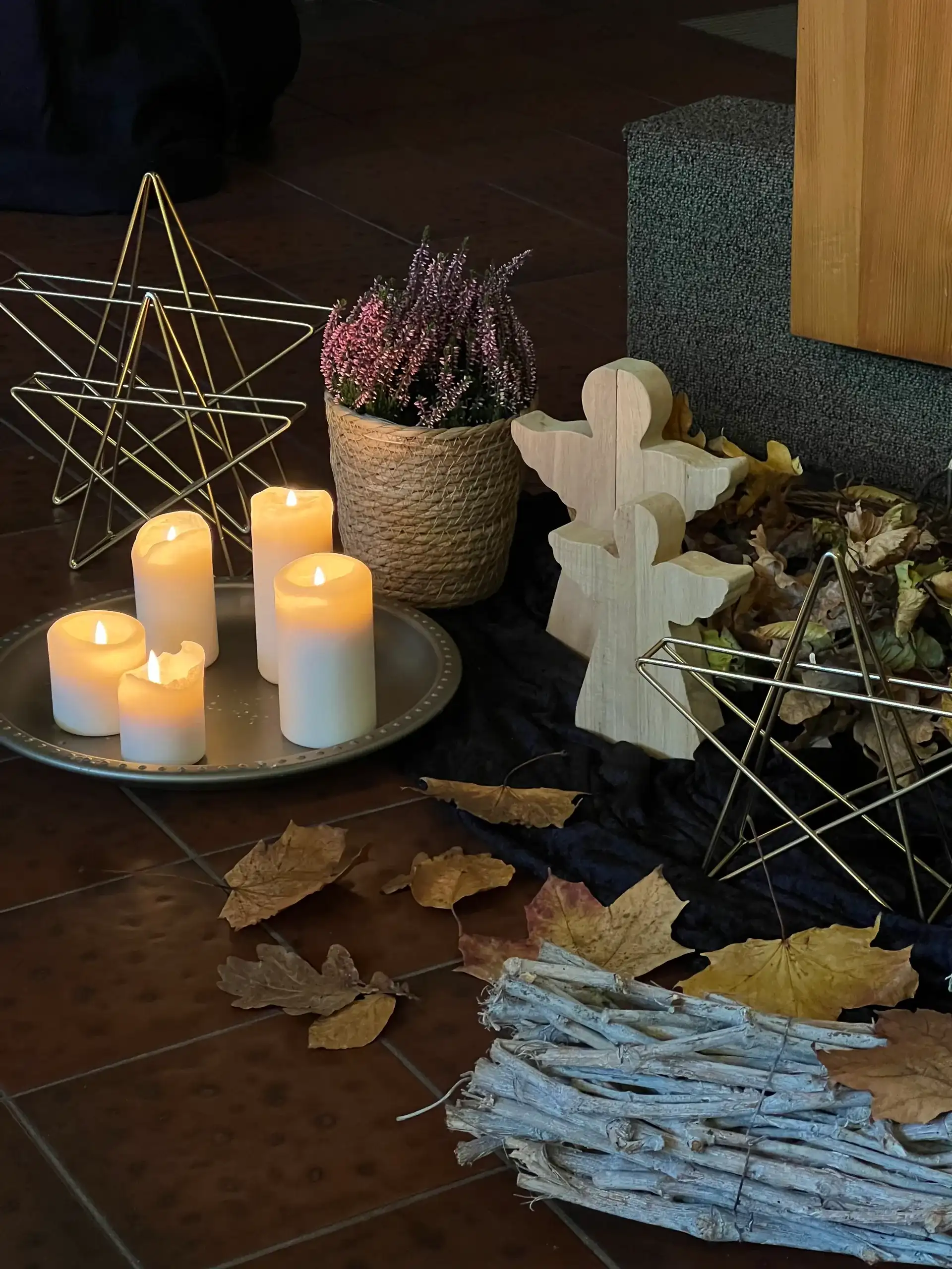 Kerzen auf einer Schale mit Heidekraut, Holzengel und Herbstlaub