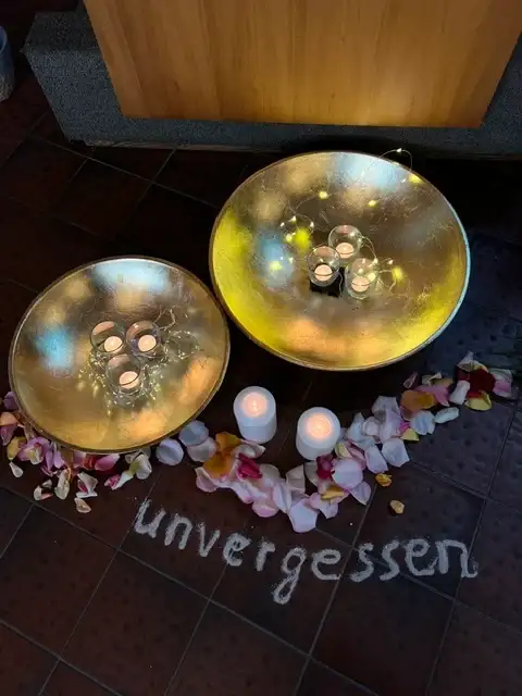 Goldene Kerzenschalen mit Blütenblättern und der Streuschrift „unvergessen“