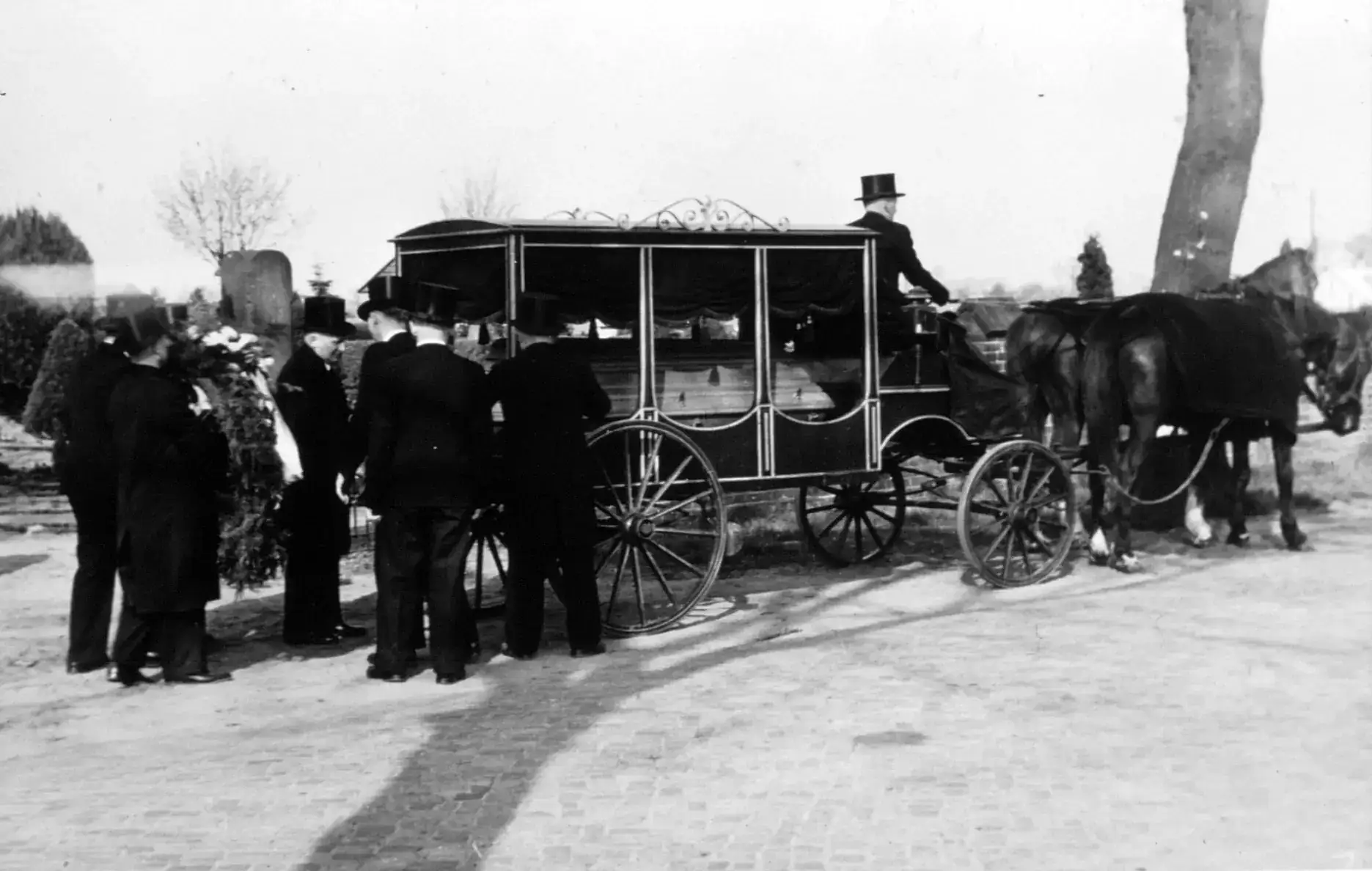 Historische Aufnahme: gläserner Leichenwagen mit Pferdegespann und Trauergästen