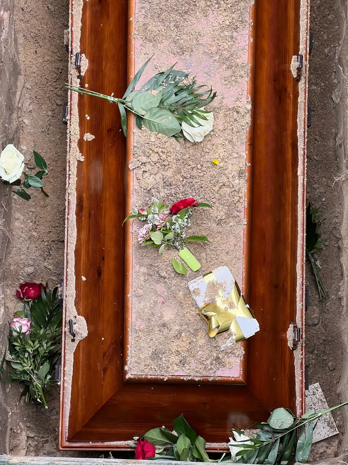 Beisetzung des Sarges im Grab, auf dem Deckel liegen Rosen und ein Blumengruß