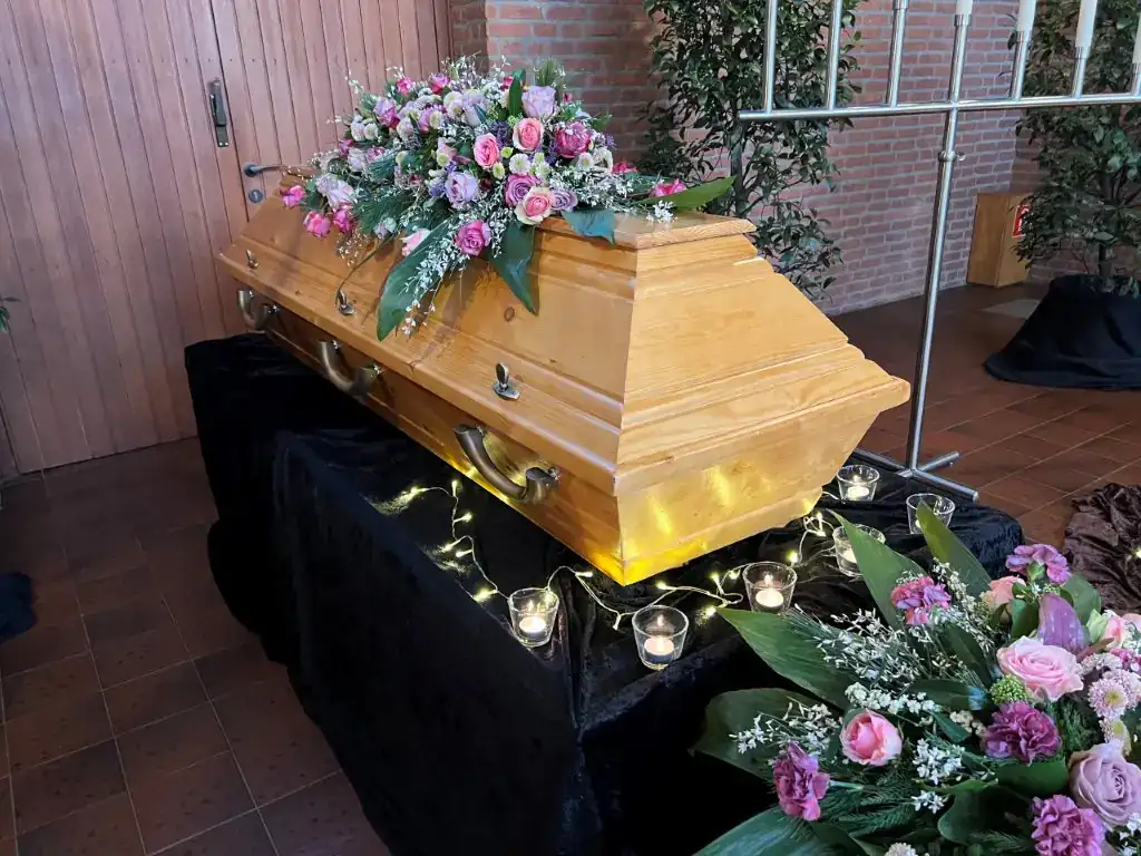 Heller Holzsarg mit Blumengesteck, Lichterkette und Teelichtern in der Trauerhalle