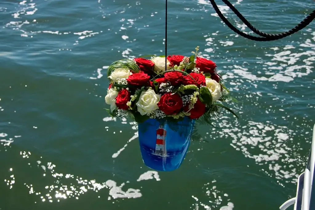 See-Urne mit Leuchtturmmotiv und rot-weißem Rosenschmuck über der Wasseroberfläche