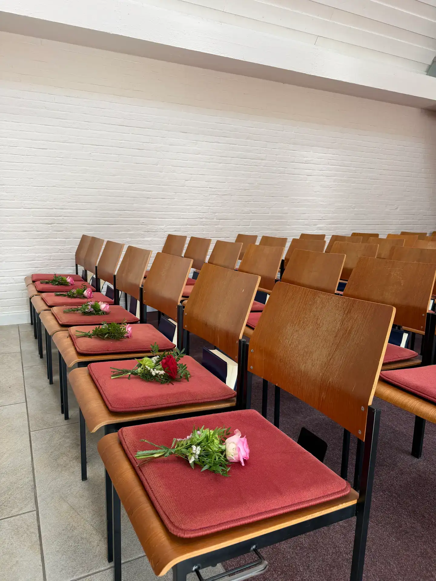 Stuhlreihen in einer hellen Trauerhalle, auf jedem Platz ein kleiner Blumengruß