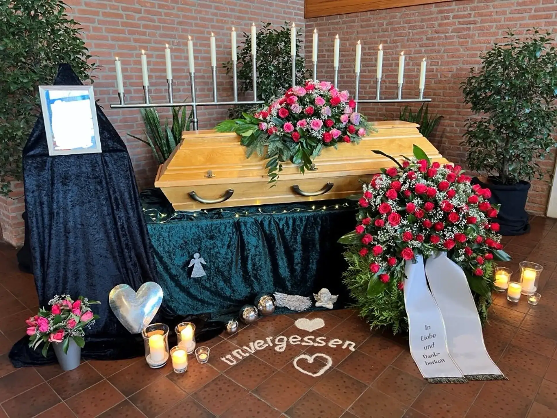 Würdevoll geschmückte Trauerhalle mit Sarg, Blumenschmuck und brennenden Kerzen