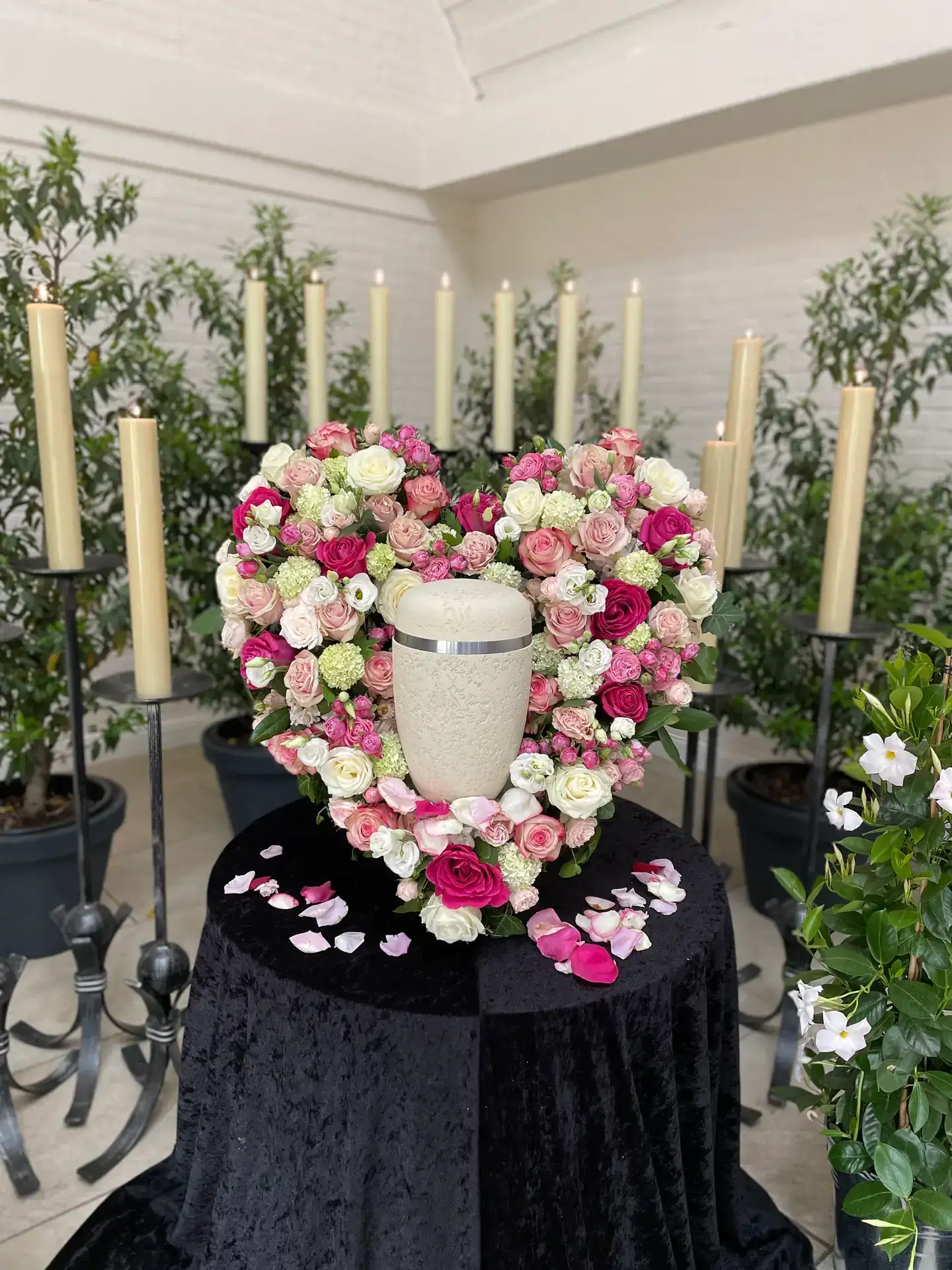 Urne in einem Herz aus rosa und weißen Rosen zwischen hohen Kerzenleuchtern