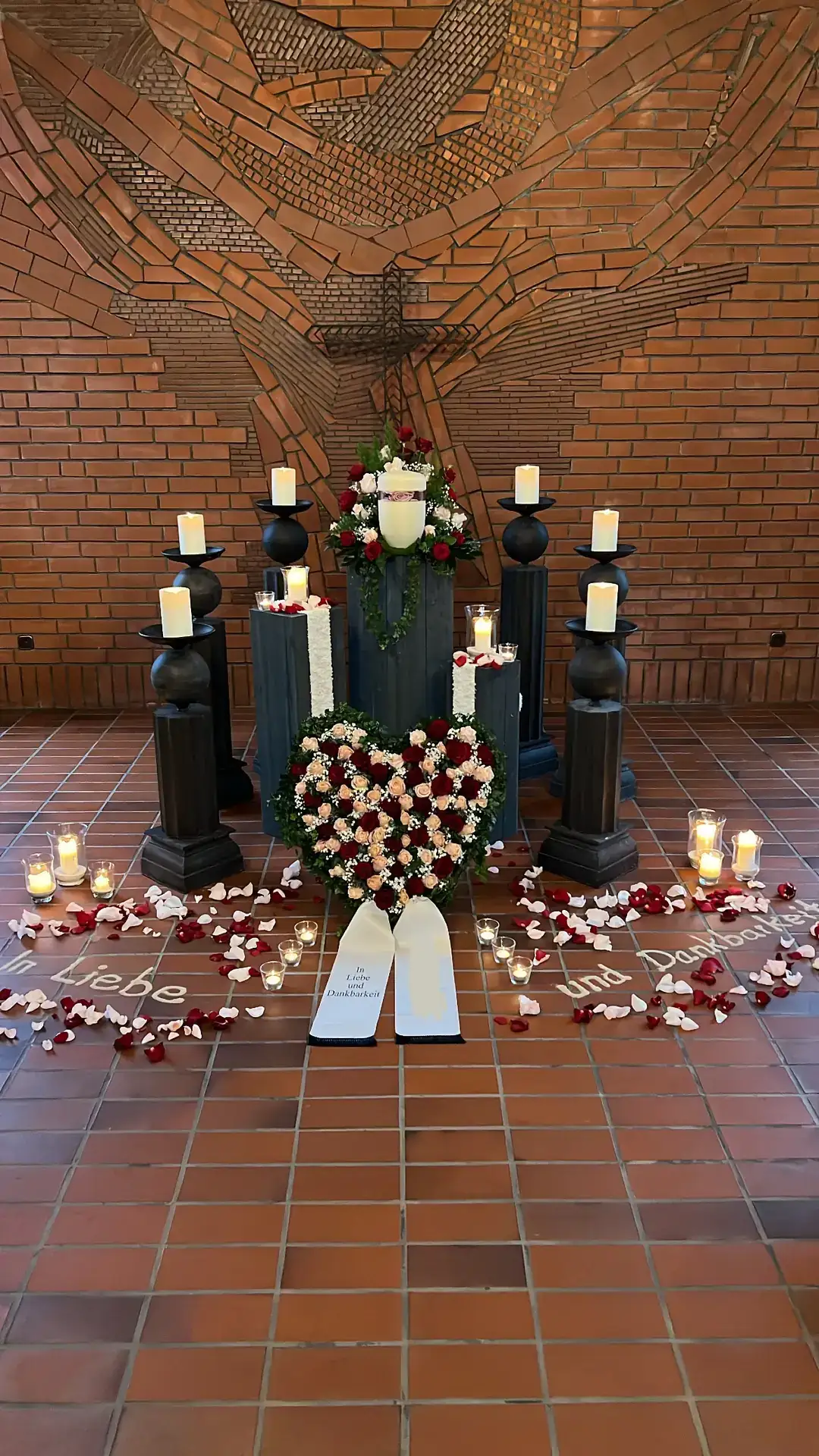 Trauerhalle mit Ziegelkreuz: Urne auf Podest, Herzgesteck, Kerzen und gestreute Rosenblätter